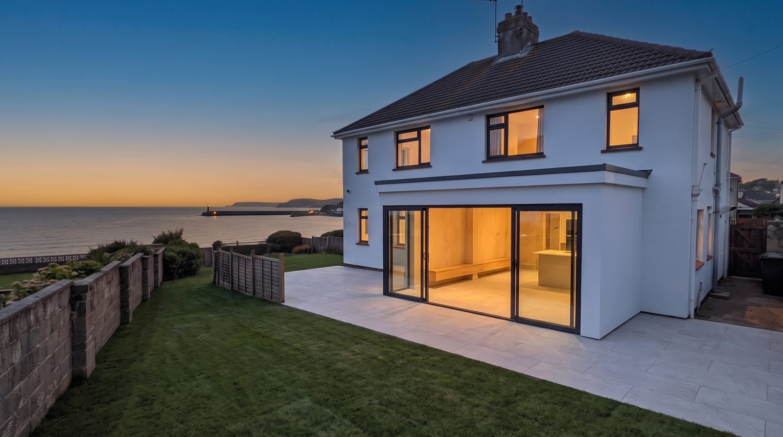 The Anthracite — white render extension with anthracite sliding glass at dusk